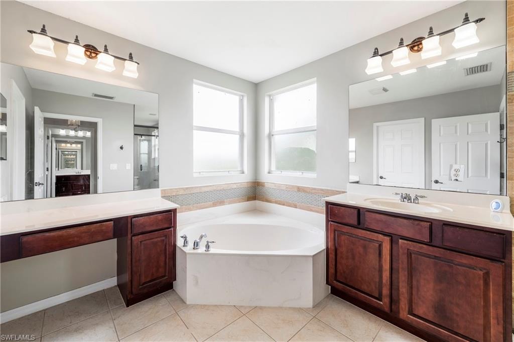 Bathroom featuring a corner soaking tub, two separate wood-finish vanities with integrated sinks, and individual wall-mounted mirrors with vanity lighting