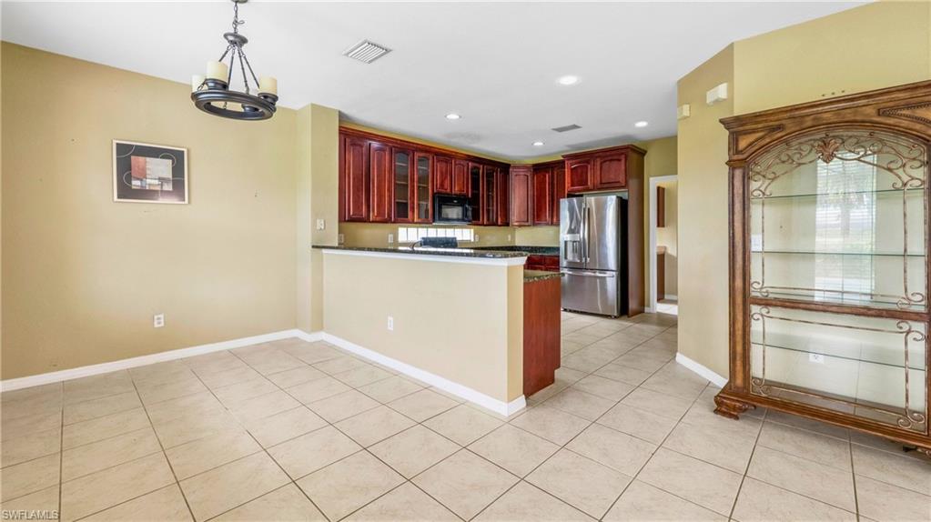 Open-concept kitchen and dining area featuring tile flooring, dark wood cabinetry, stainless steel appliances, recessed lighting, and a breakfast bar