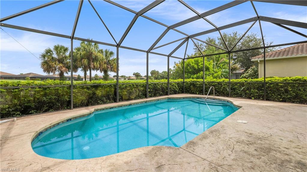 Screened outdoor pool area featuring a freeform pool with integrated steps, surrounded by a textured concrete deck