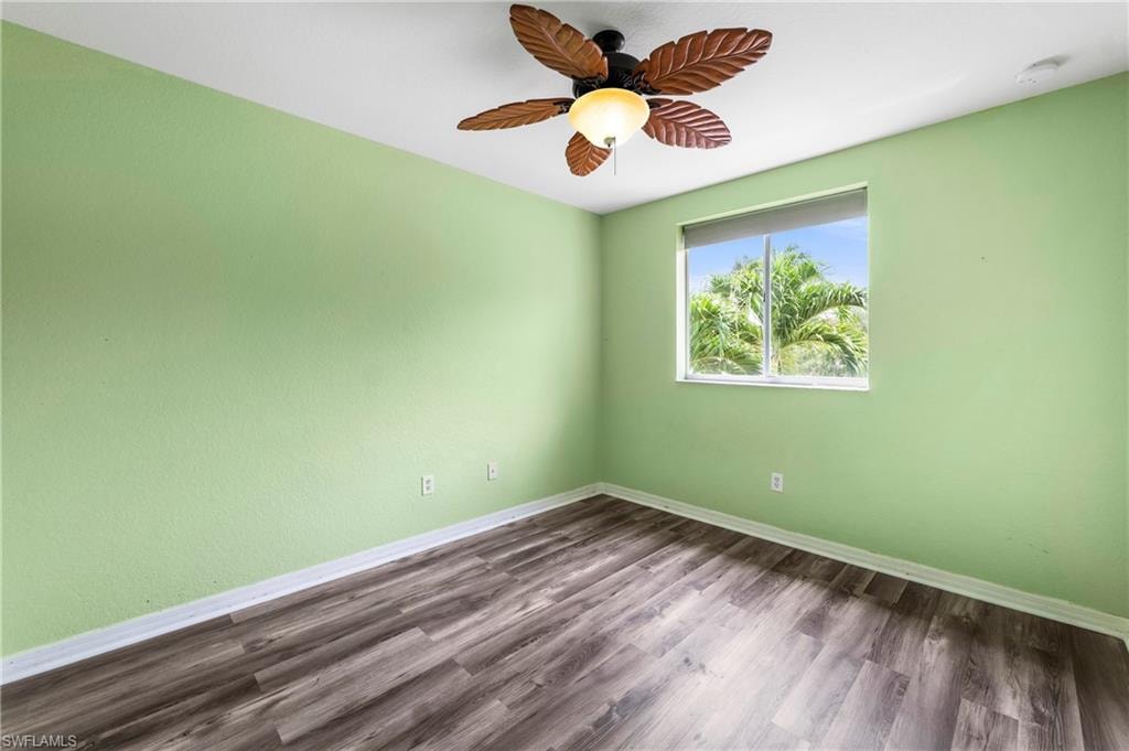 Room featuring wood-finish flooring, a single window, and a ceiling fan with leaf-shaped blades