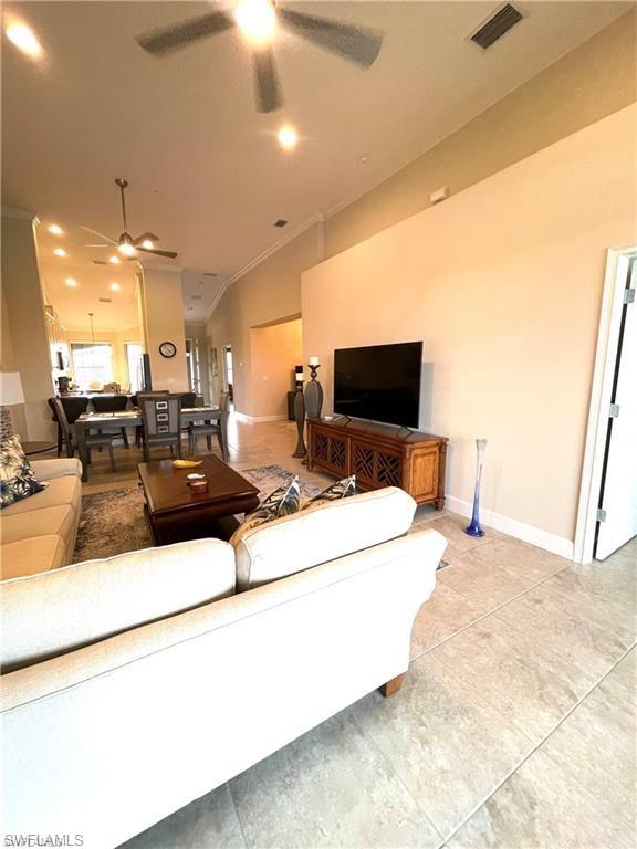 Living area featuring lofted ceiling, visible vents, baseboards, and ceiling fan
