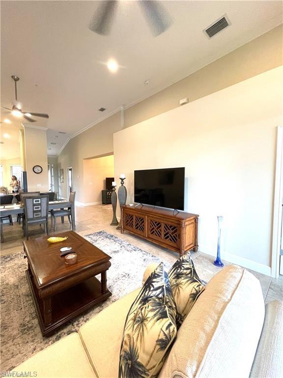 Living room with baseboards, ornamental molding, a ceiling fan, visible vents, and lofted ceiling