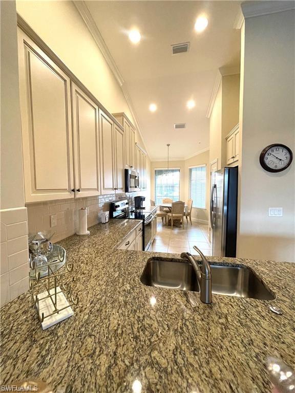 Kitchen featuring backsplash, crown molding, visible vents, stainless steel appliances, and a sink