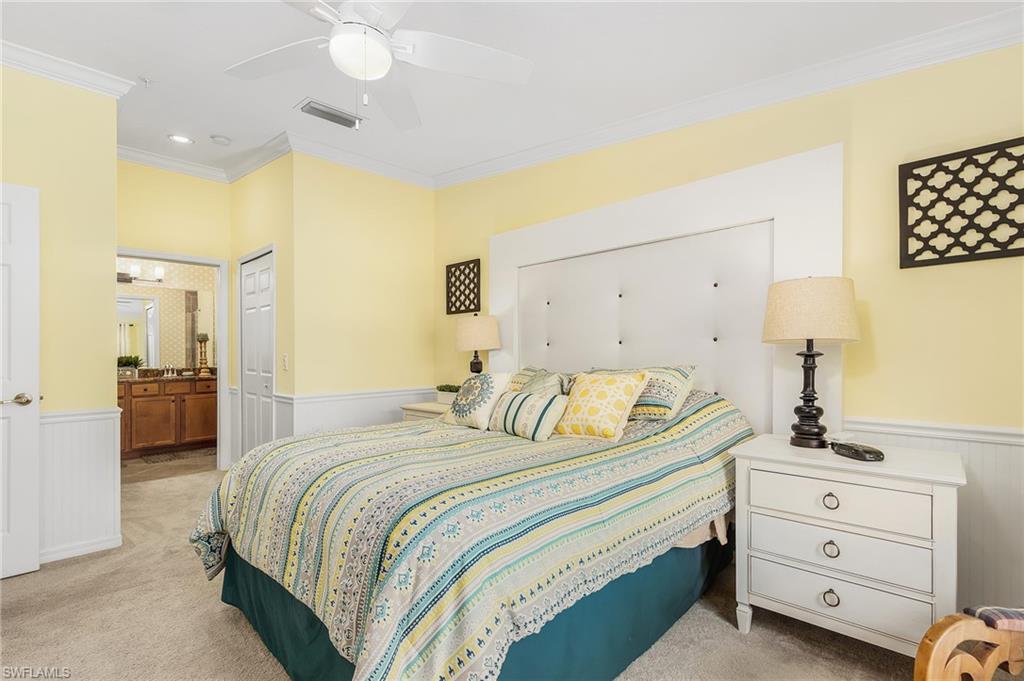 Bedroom featuring a wainscoted wall, light colored carpet, crown molding, a ceiling fan, and ensuite bath