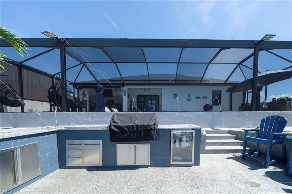 Outdoor entertainment area featuring a screened enclosure, built-in outdoor kitchen with integrated stainless steel appliances, stone-look countertops, and blue tile detailing