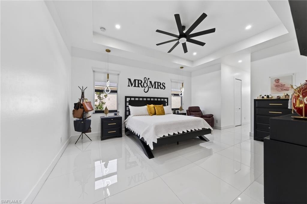 Spacious room featuring white tile flooring and a tray ceiling with a contemporary ceiling fan