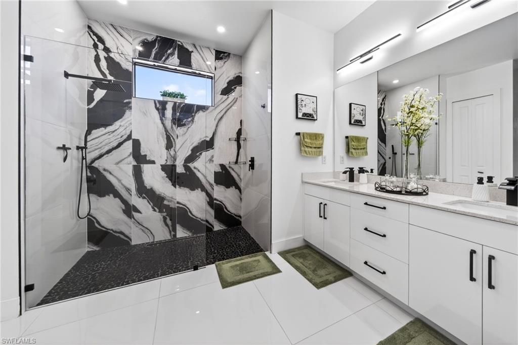 Modern primary bathroom featuring a spacious walk-in shower with black and white patterned wall tiling, a rectangular window, and a pebble-finish shower floor