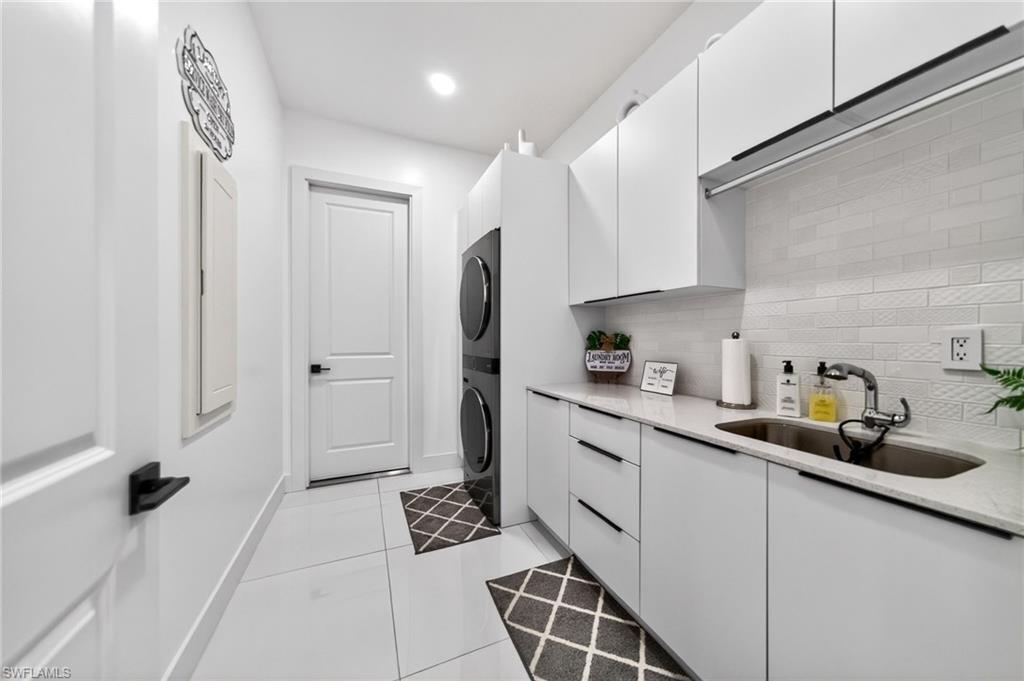 Dedicated laundry area featuring a stacked washer and dryer, white shaker-style cabinetry, and a countertop with an integrated sink, and build in iron table