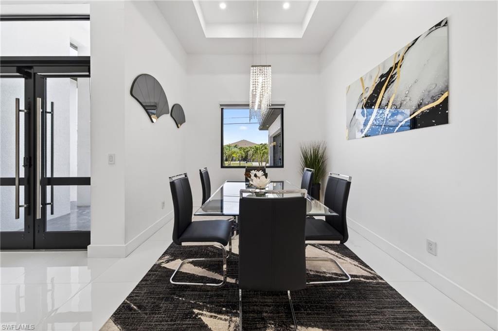 Recessed ceiling with an elegant chandelier over a dining area featuring white tile flooring and a large picture window