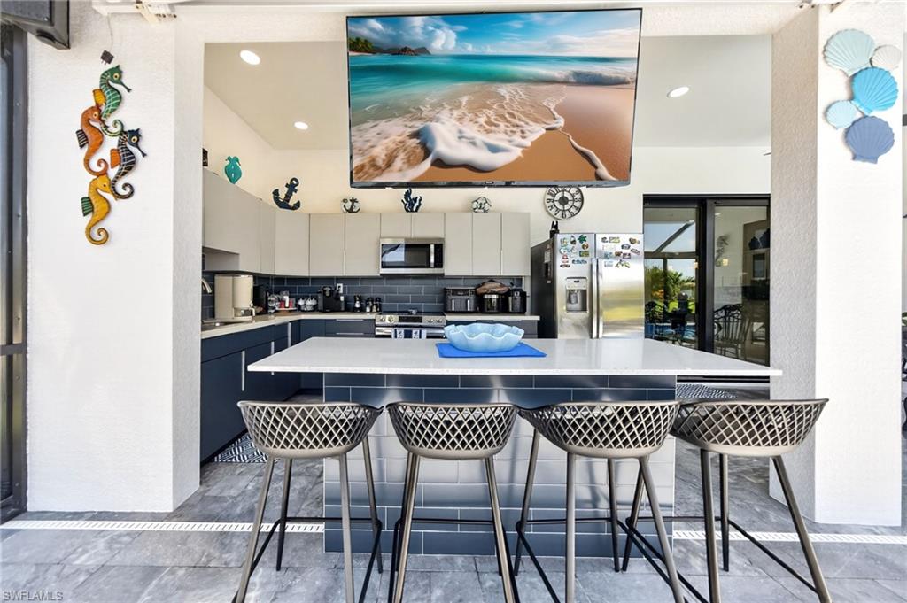 Outdoor kitchen featuring an expansive white countertop island with integrated seating, gray subway tile backsplash, recessed lighting, and stainless steel appliances