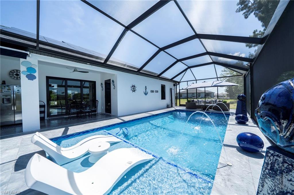 Screened pool enclosure featuring a rectangular pool with water features, a covered patio with ceiling fan, and large sliding glass doors