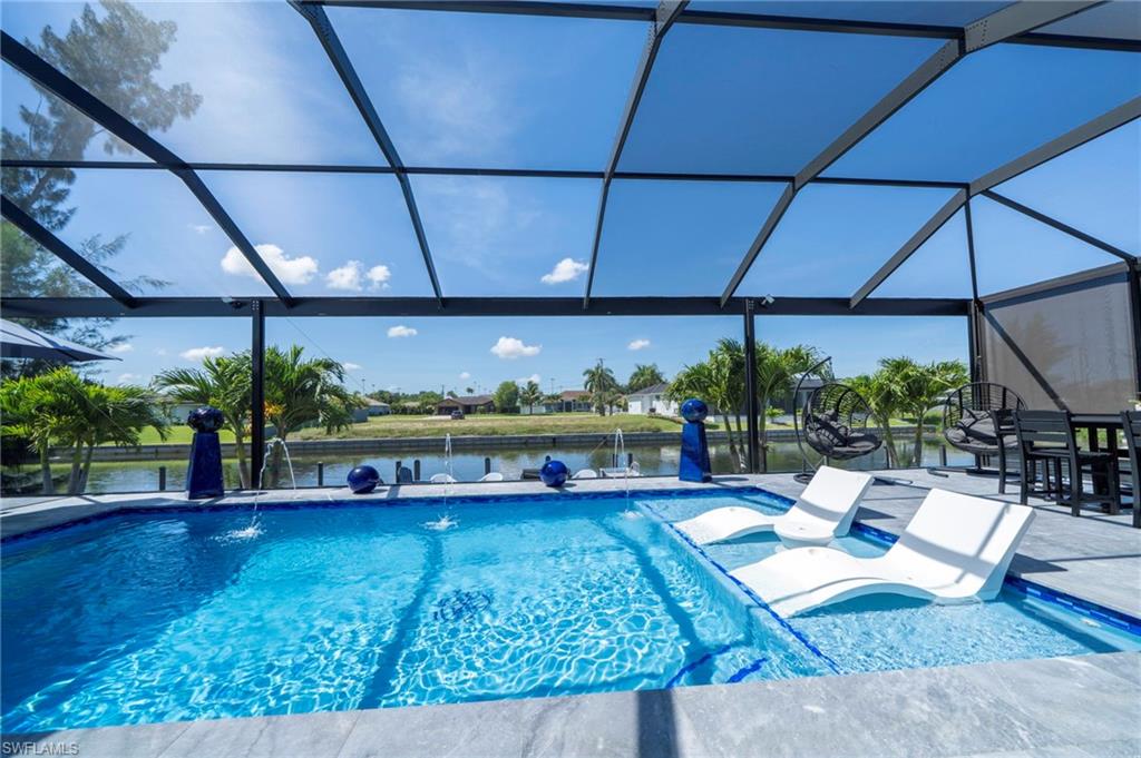 Screened-in pool deck featuring a swimming pool with integrated sun shelf, water features, and expansive paver decking