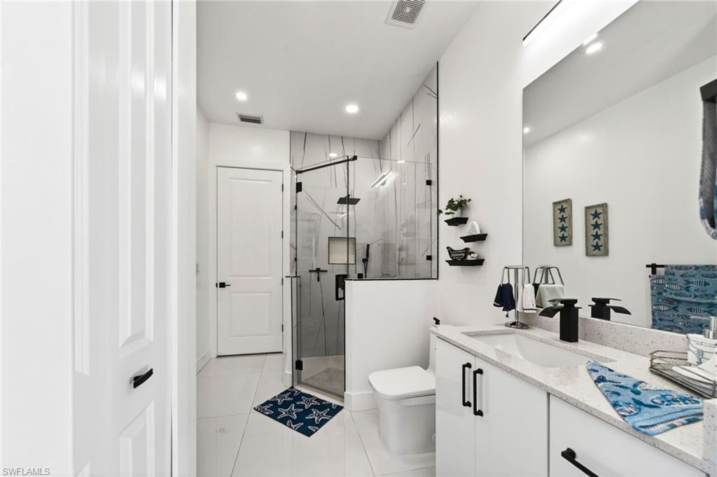 Modern 2nd bedroom bathroom featuring a frameless glass shower enclosure with matte black hardware, a floating vanity with a light-toned countertop, and white tile flooring, with pool access