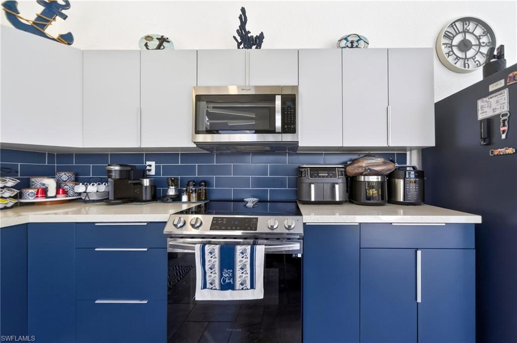 Kitchen featuring two-tone cabinetry with blue lower and light upper cabinets, complementing blue subway tile backsplash, and light-toned countertops