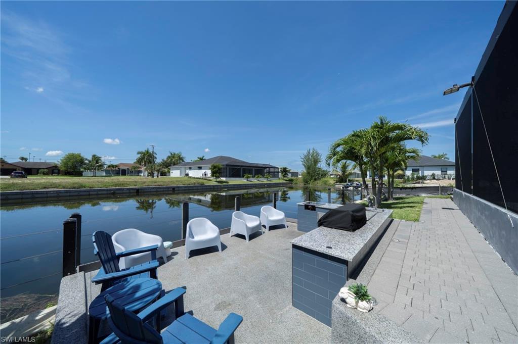 Waterfront patio featuring a built-in outdoor kitchen with a stone countertop, a spacious paved patio area, and mature palm trees