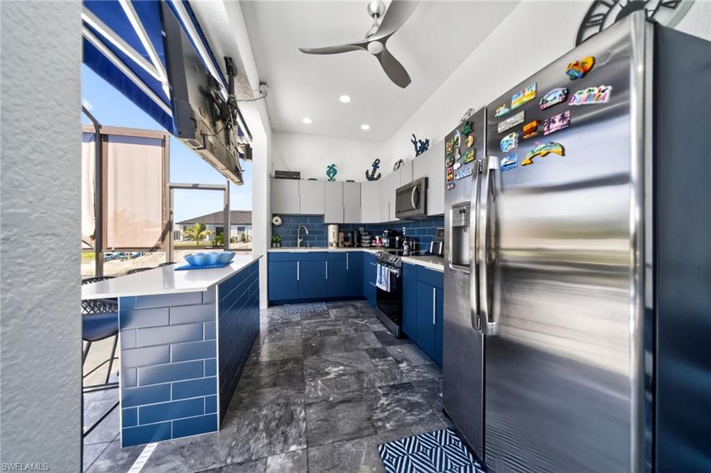 Outdoor kitchen featuring stainless steel appliances, blue subway tile backsplash, white countertops, and a ceiling fan