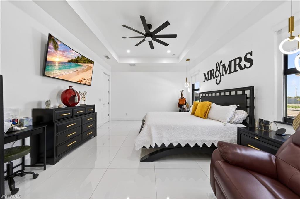 Spacious bedroom with white tile flooring and a tray ceiling