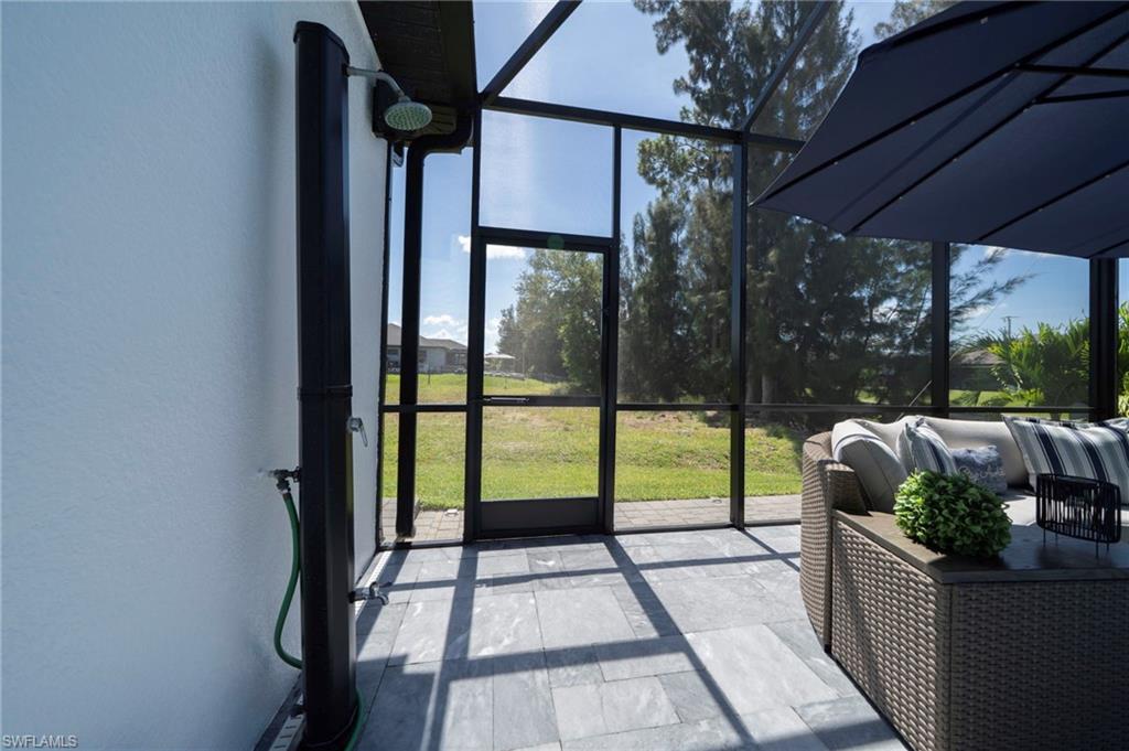 Screened-in outdoor living space featuring dark frame construction, gray stone-look flooring, and a wall-mounted outdoor shower fixture