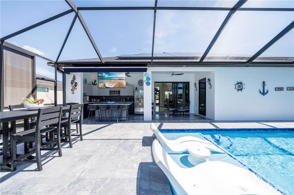 Screened outdoor living area featuring a swimming pool with integrated seating, a built-in outdoor kitchen with bar seating, and ample patio space with large format tile flooring