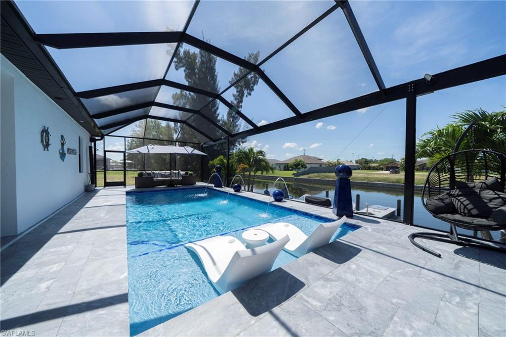 Screened outdoor living area featuring a rectangular pool with integrated shallow lounging area, light-toned tile decking, and a canal-front setting with a private dock