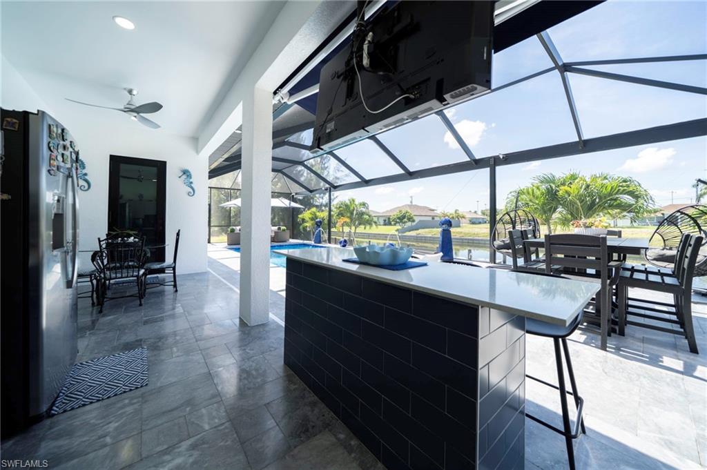 Screened patio featuring a swimming pool, canal access, a built-in bar with dark tile, a recessed ceiling fan, and large format tile flooring