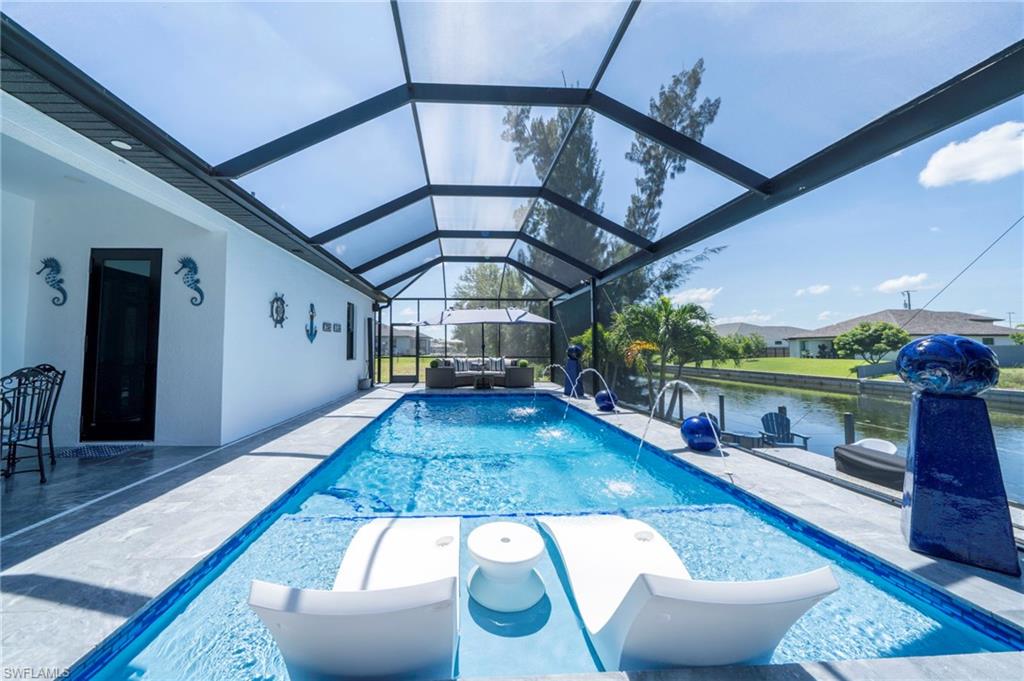 Screened swimming pool with integrated sun shelf, multiple water features, and a view of the adjacent canal