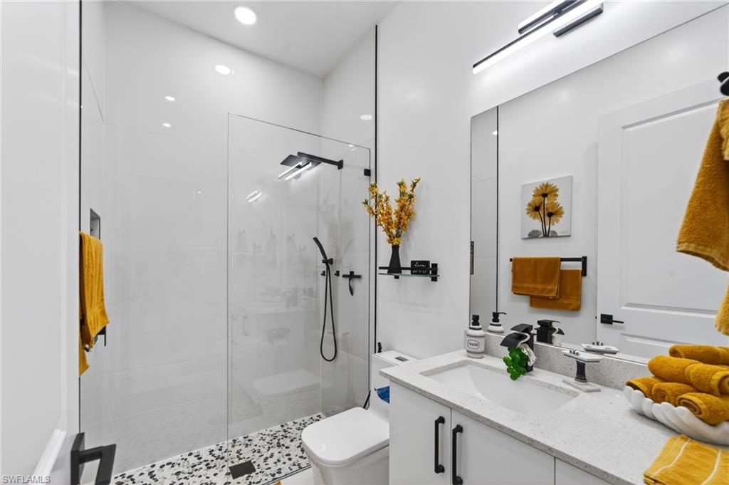 Contemporary guest bathroom featuring a frameless glass shower enclosure, black pebble tile shower floor, and a white vanity with a light-colored countertop