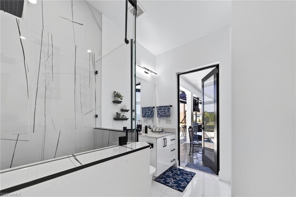 Modern 2-bedroom, bathroom featuring a glass-enclosed shower with large format tile, a rain shower head, and a sleek black framed vanity mirror, with pool access