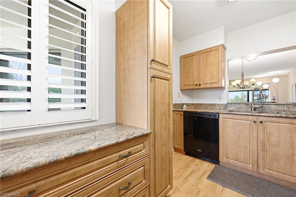 Kitchen featuring light wood-finish cabinetry, speckled countertops, stainless steel sink, and a black dishwasher