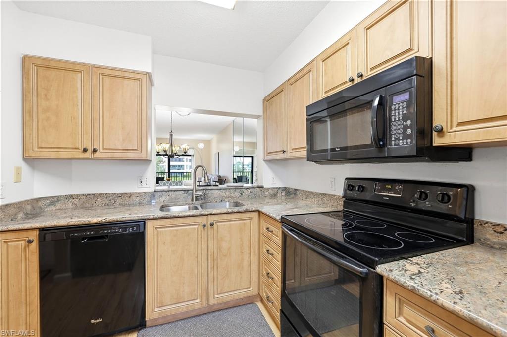 Kitchen featuring light wood cabinetry, granite-patterned countertops, and a full suite of black appliances, including an electric range with an overhead microwave