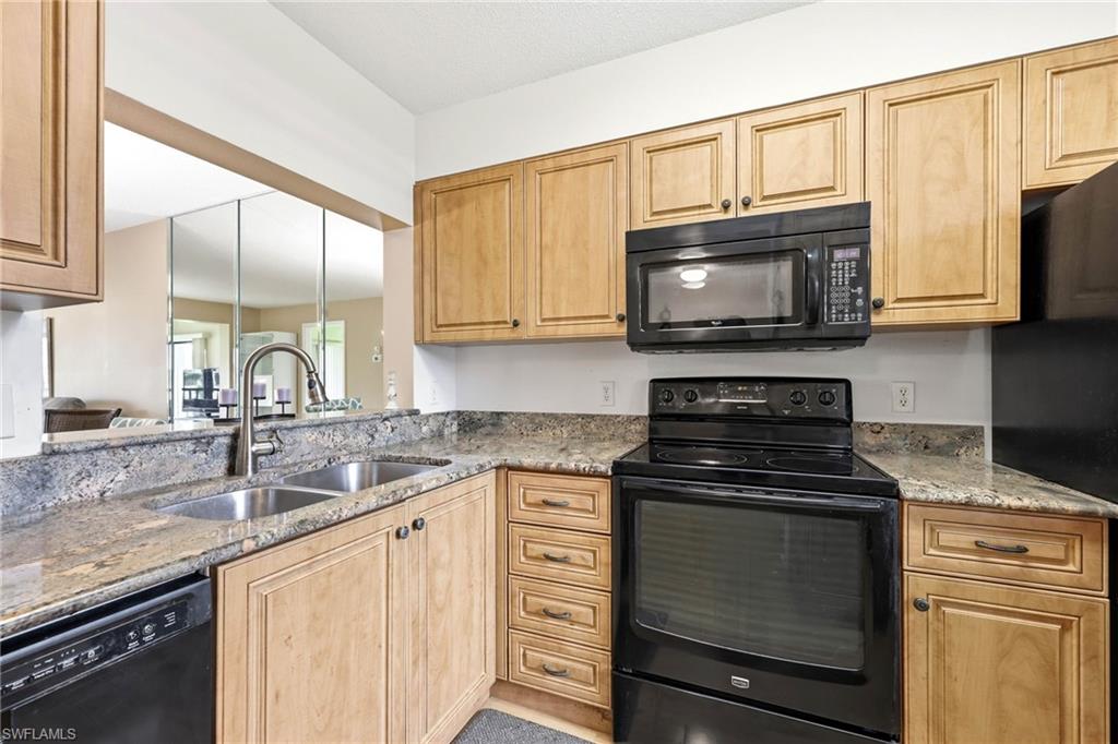 Kitchen featuring wood cabinetry, stone countertops, double basin stainless steel sink, black electric range, and black built-in microwave