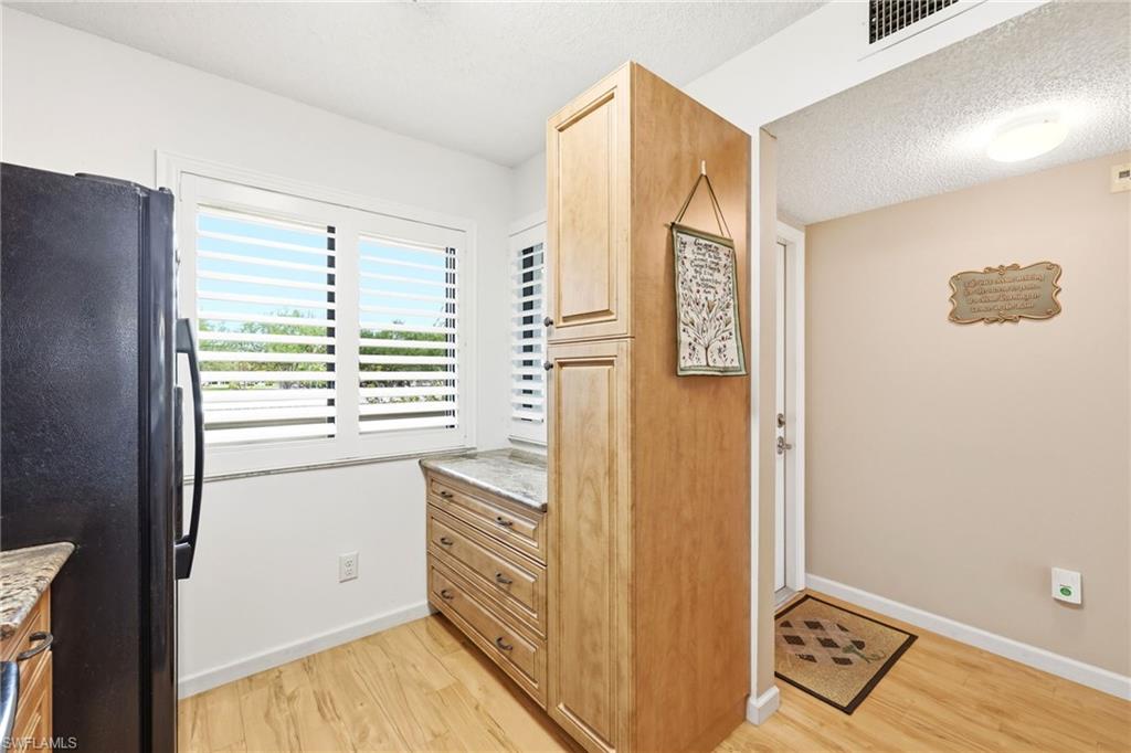 Kitchen area featuring light wood-finish flooring, a built-in cabinet with multiple drawers and a countertop, and a window with plantation shutters