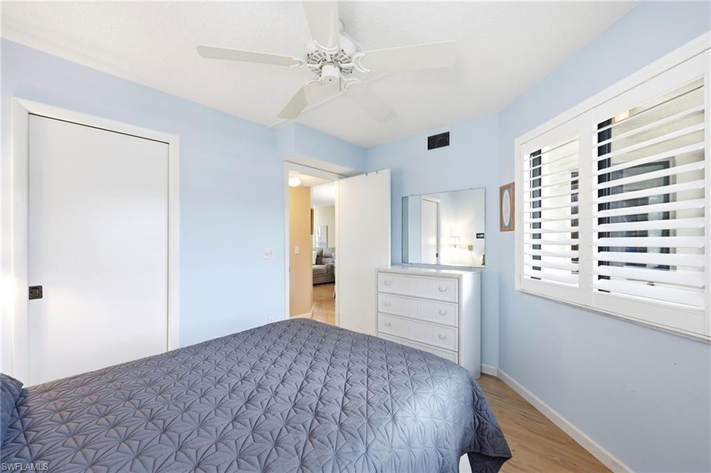 Bedroom featuring wood-finish flooring, a ceiling fan, and window with plantation shutters