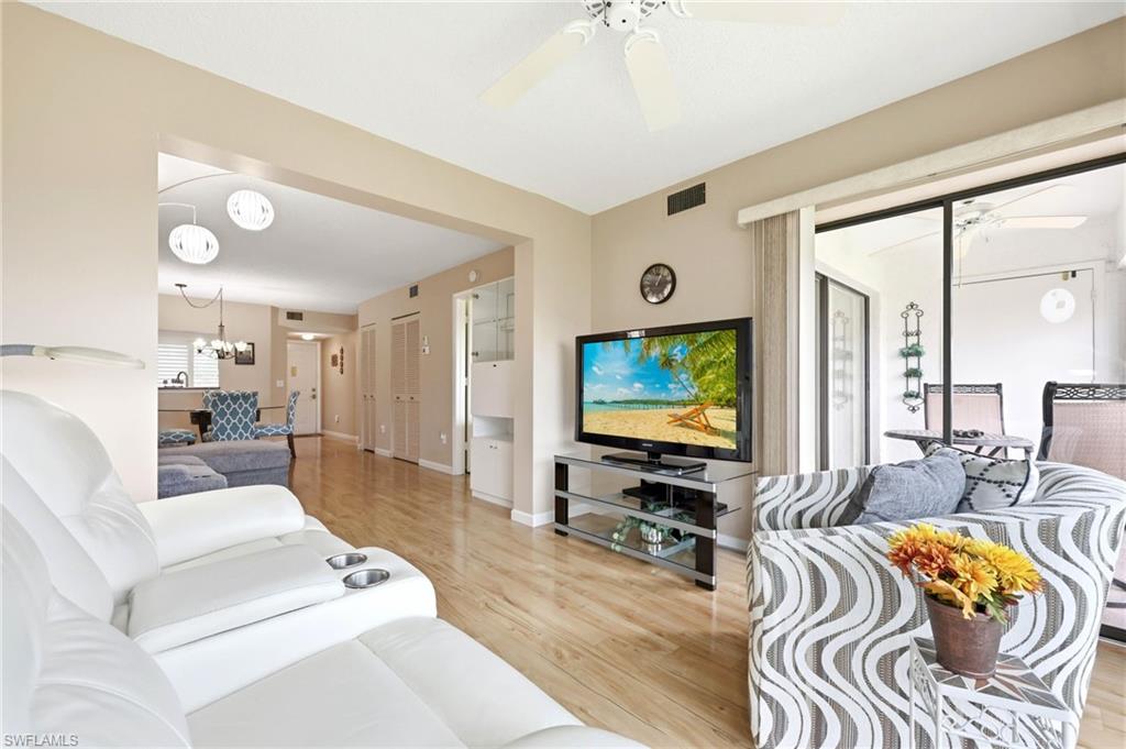 Spacious living area featuring light wood-finish flooring, a ceiling fan, and sliding glass doors opening to an outdoor patio