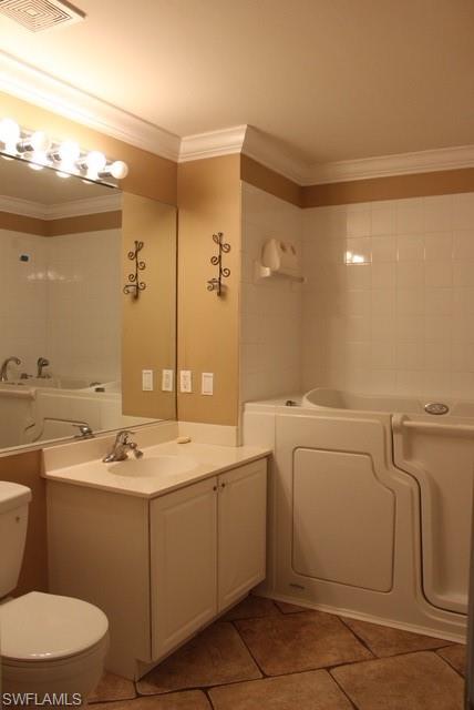 Bathroom featuring a walk-in tub, white vanity with integrated sink, white toilet, and textured floor tiles