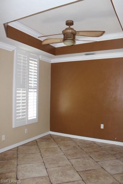 Room featuring a tray ceiling with a ceiling fan, crown molding, plantation shutters, and large format floor tiles