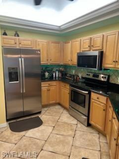 Kitchen featuring warm-toned cabinetry, stainless steel appliances, dark countertops, and a green tile backsplash