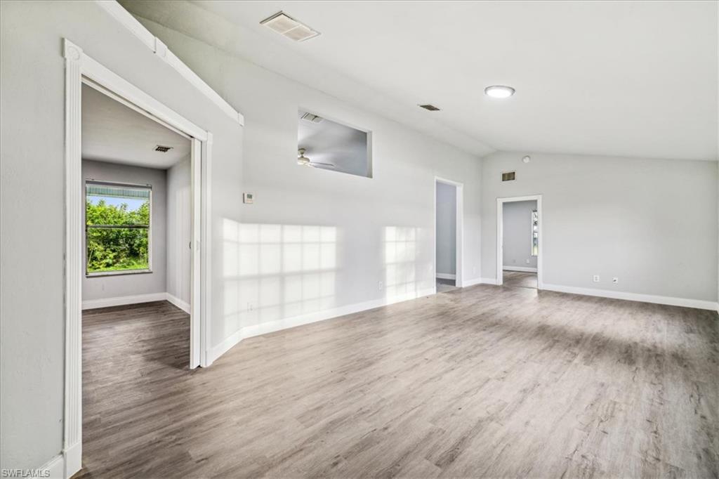 Empty room with lofted ceiling, ceiling fan, and dark wood-type flooring