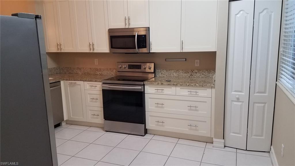 Kitchen featuring white cabinetry, light tile patterned flooring, light stone countertops, and appliances with stainless steel finishes