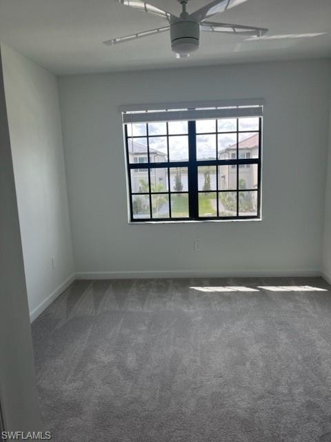 Spare room featuring a ceiling fan, healthy amount of natural light, dark carpet, and baseboards