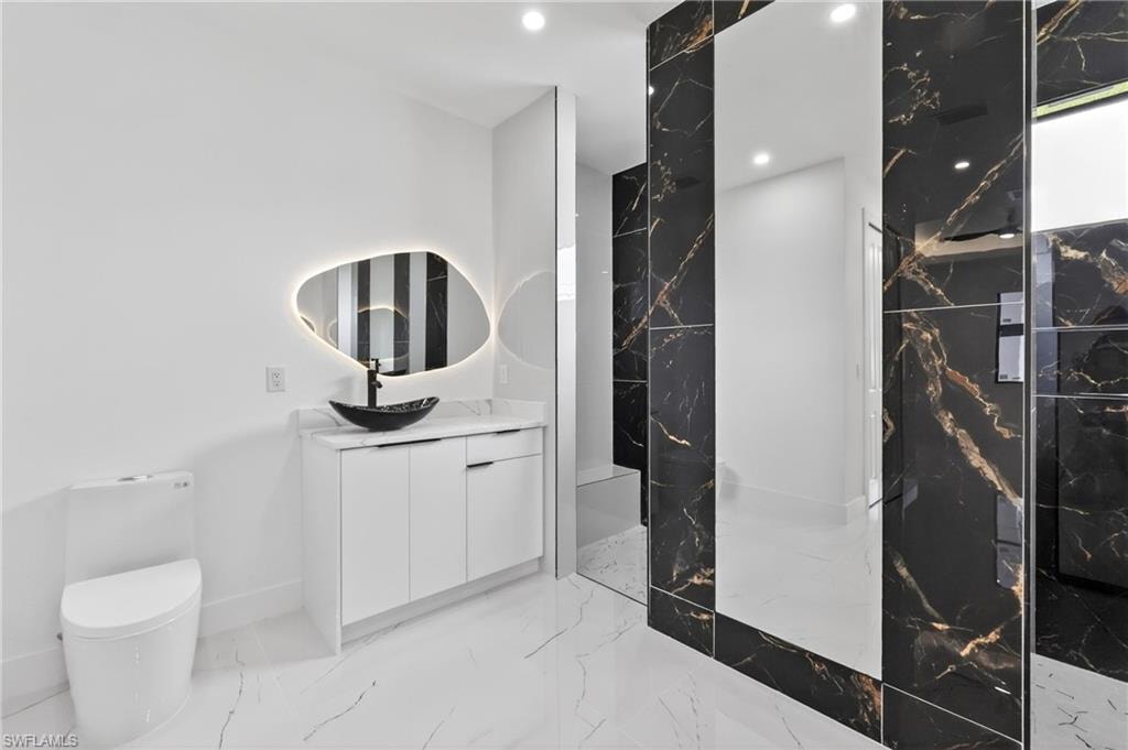 Modern bathroom featuring a white vanity with a rectangular countertop, a vessel sink, and a backlit irregular-shaped mirror