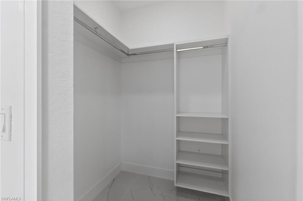 Walk-in closet featuring white walls, baseboards, marble-look tile flooring, chrome hanging rods, and integrated shelving