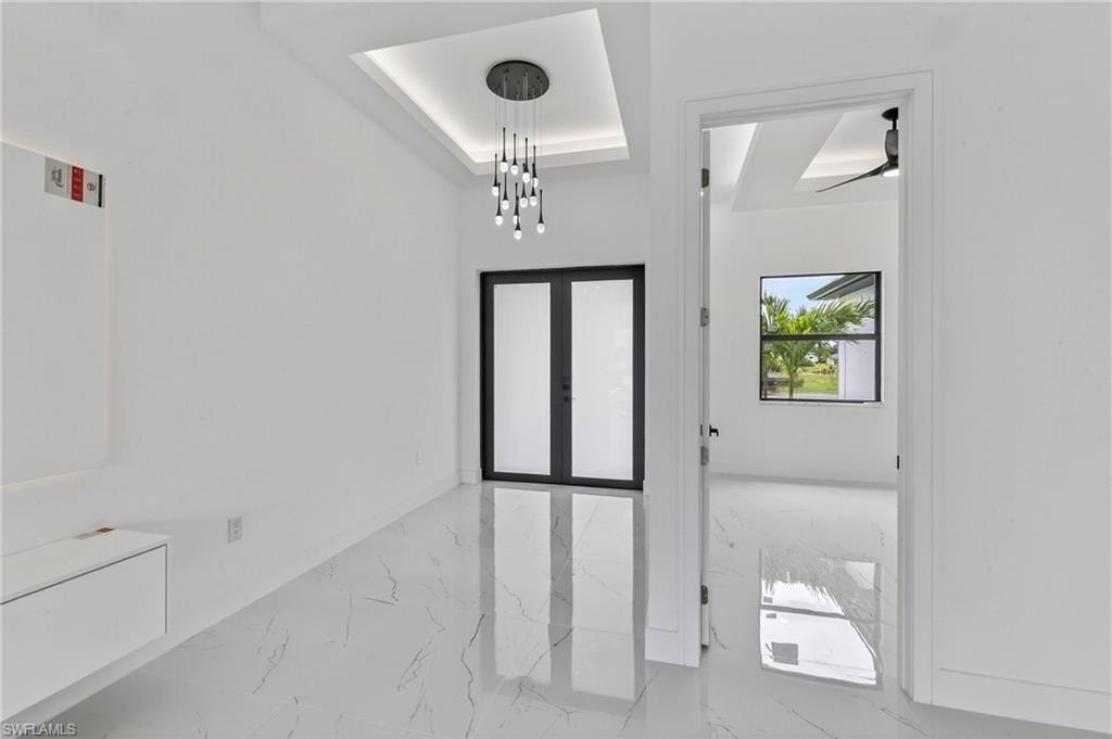 Entryway featuring large format tile flooring, a modern chandelier with multiple pendants, and tray ceiling with recessed lighting