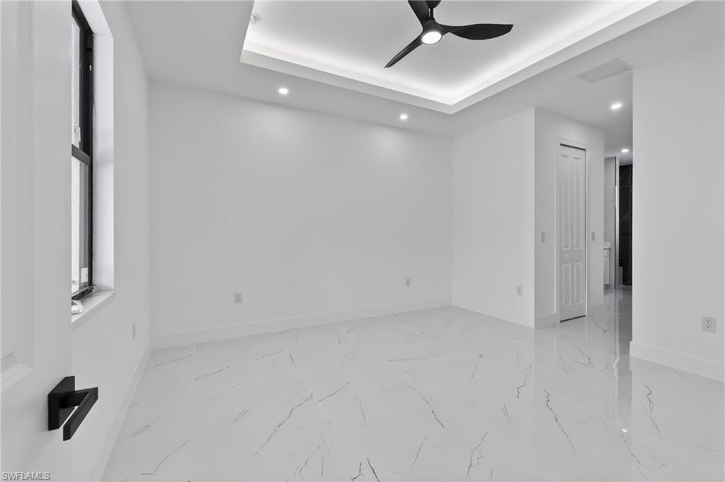 Spacious room featuring white tile flooring, a tray ceiling with recessed lighting, and a modern ceiling fan