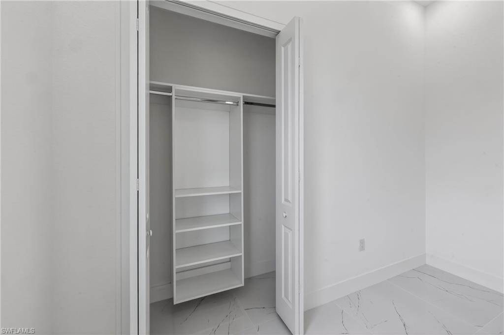 Interior closet with built-in shelving unit, clothing rod, bi-fold door, white baseboards, and marble-look tile flooring