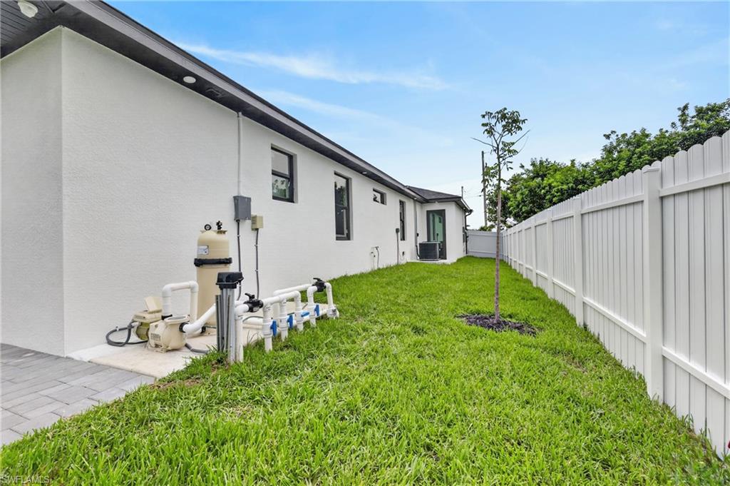 Expansive side yard featuring a white privacy fence, green lawn, and a young tree
