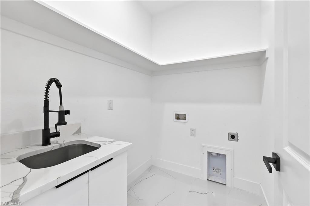Dedicated laundry space featuring a matte black pull-down faucet, undermount sink, stone-finish countertop, white cabinetry with linear pulls, and coordinated tile flooring