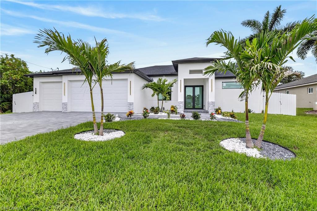 Contemporary exterior featuring a white stucco finish, a double-door entry, a two-car garage, manicured landscaping, and twin palm trees