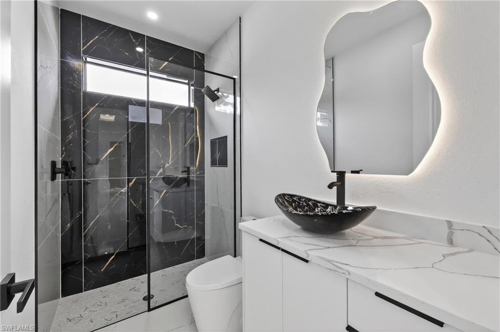 Modern bathroom featuring a glass-enclosed shower with black-veined wall tile, a transom window, and a rainfall showerhead