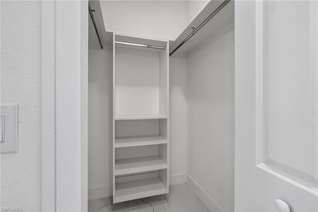 Walk-in closet featuring built-in shelving, two hanging rods, white walls, and a light-toned flooring